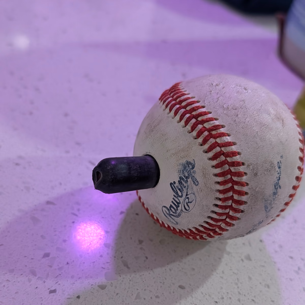 A baseball with the redesigned black cap fitted into its side, resting on a countertop