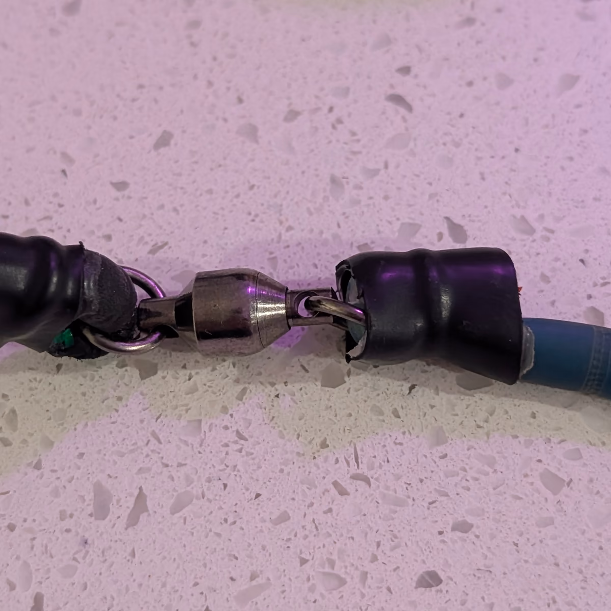 Close-up of the steel swivel joining the black woven cord to the blue latex tube, each end capped in black shrink tubing